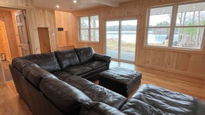 A room with a sectional sofa, wooden walls, and large windows overlooking a body of water.