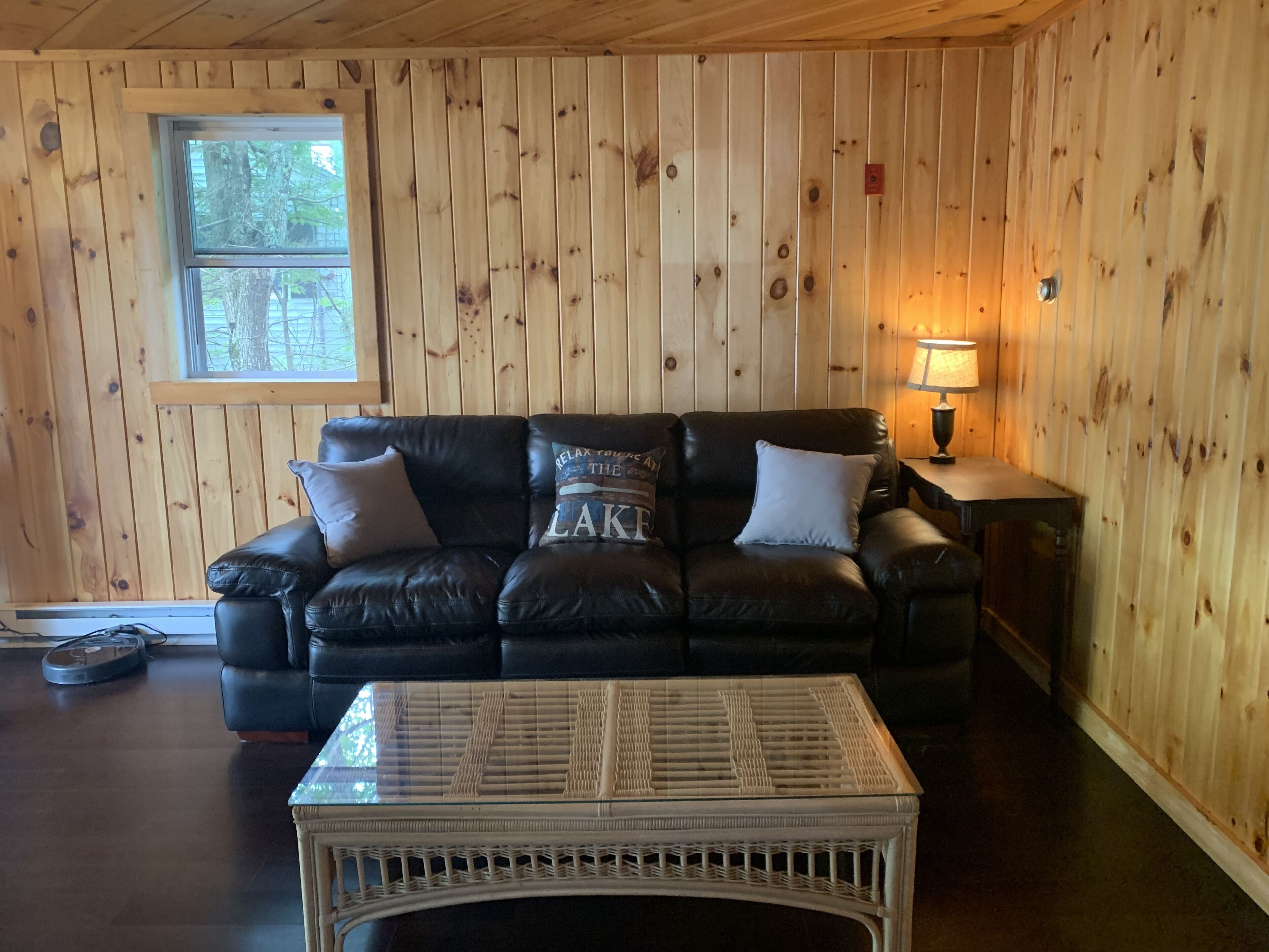 A cozy room with a black leather sofa, a wicker coffee table, and wooden paneled walls.