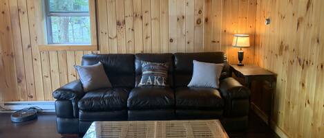 A cozy room with a black leather sofa, a wicker coffee table, and wooden paneled walls.
