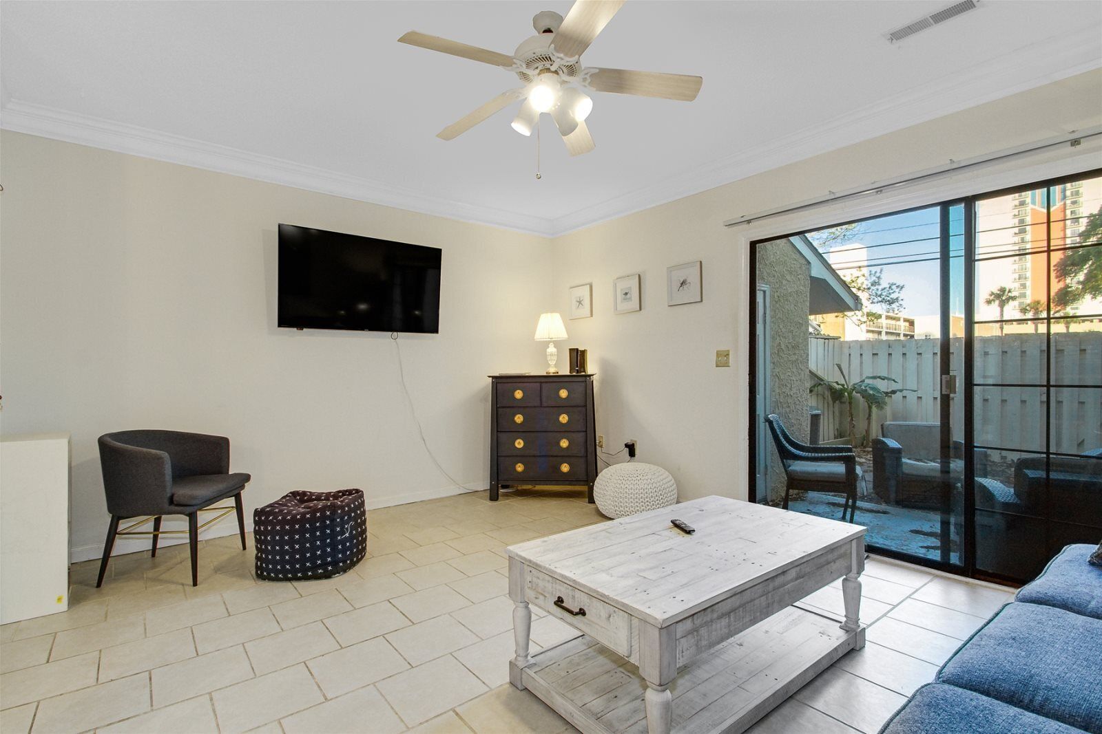 A living room with a ceiling fan, a flat-screen TV, a sofa, a coffee table, a chair, a cabinet, and a glass door leading outside.