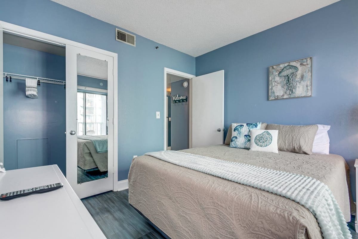 A bedroom with a bed, a bedside table, a door, and a wall with a picture.