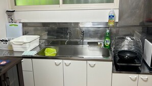A kitchen with white cabinets, a stainless steel sink, and a microwave. There is a green bottle of dish soap and a white plastic container on the counter. - Kohan no yado Kojima (Toyako)