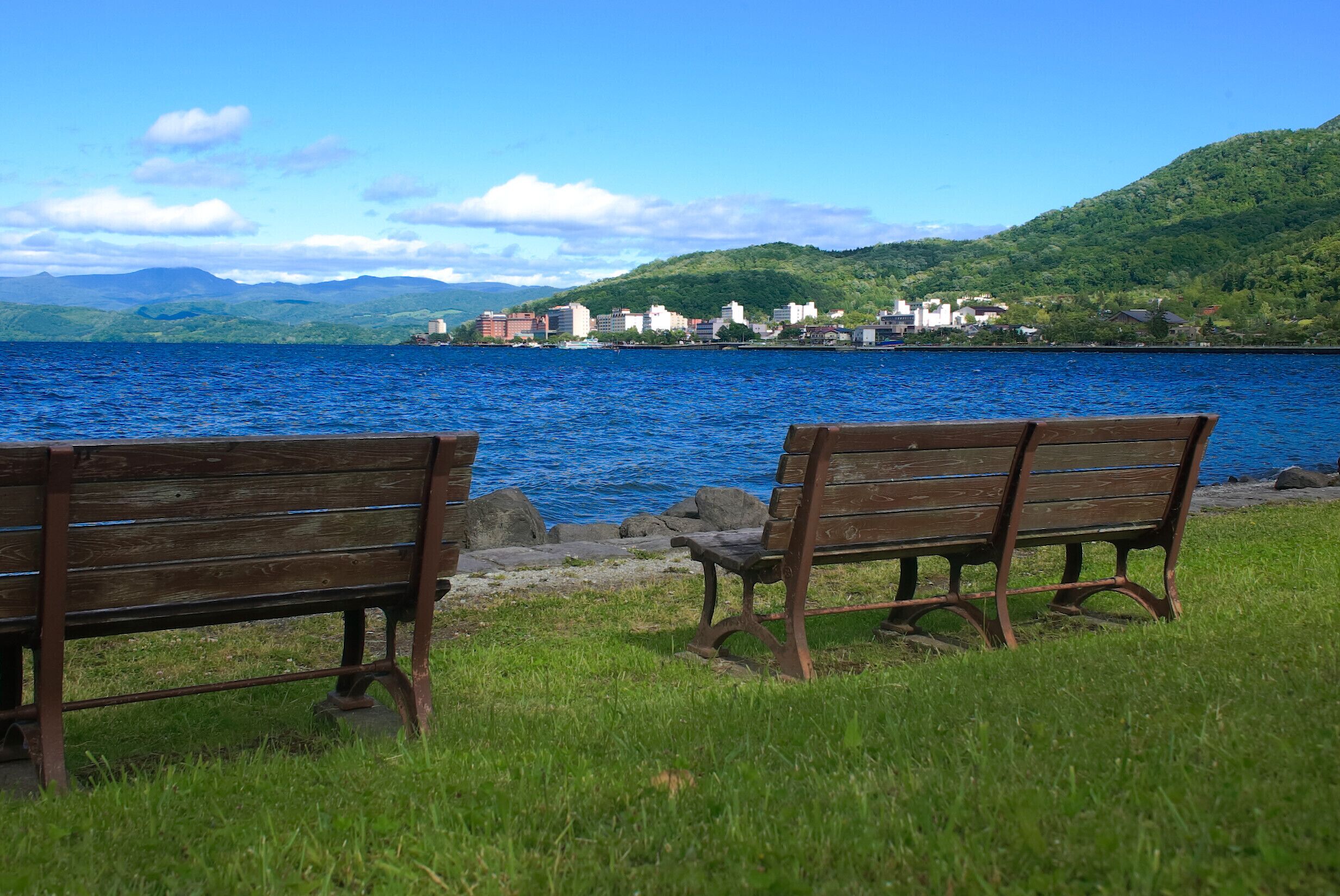 Two wooden benches facing a body of water with a cityscape in the background.