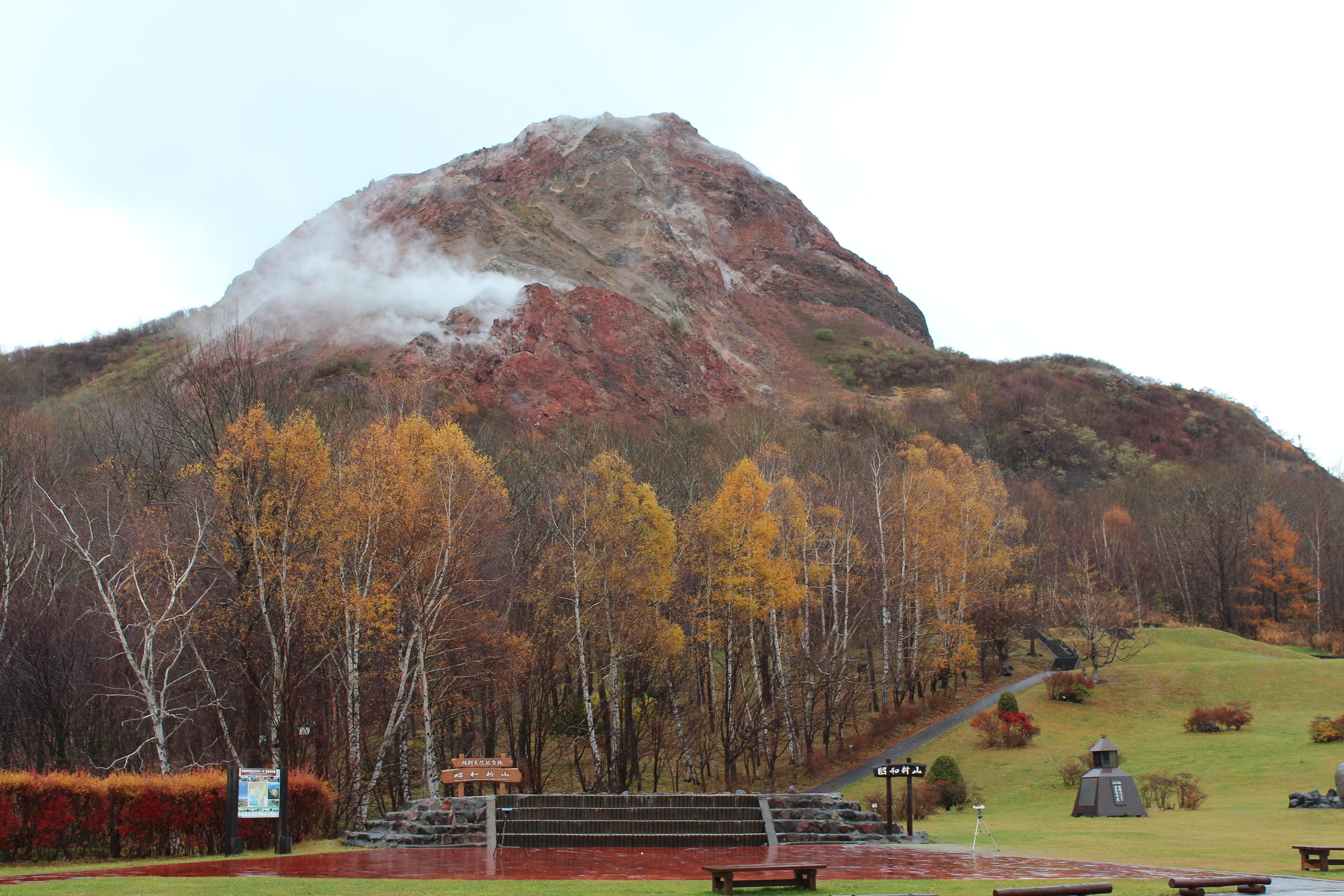 A mountainous landscape with autumn foliage, a picnic area, and a small structure on the hill.
