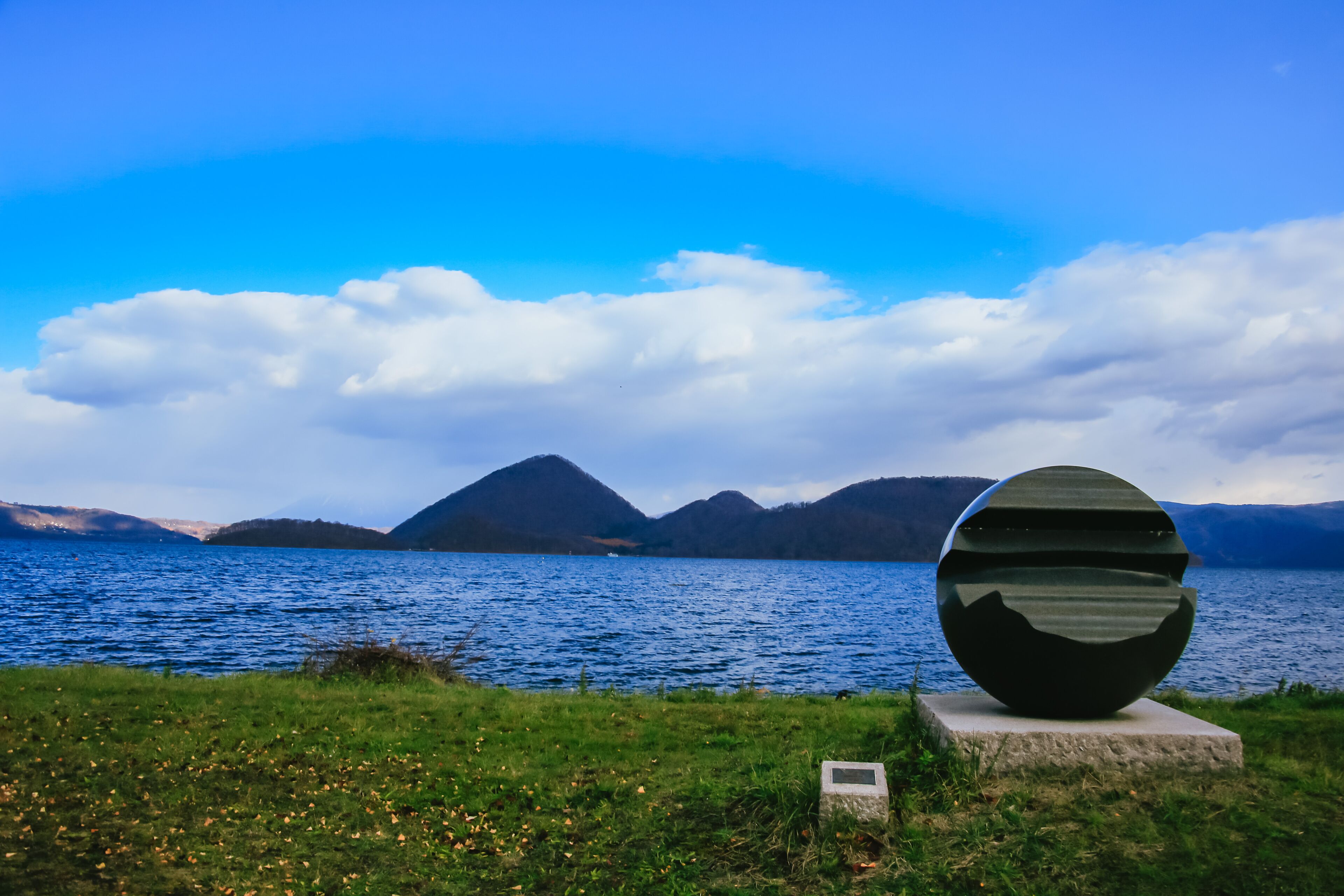 A sculpture by a lake with mountains in the background.