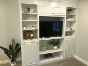 Un mueble blanco para entretenimiento con un televisor de pantalla plana, repisas con adornos y una planta en maceta.