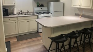 Una cucina moderna con mobili bianchi, un'isola centrale con sgabelli da bar, un piano cottura e un frigorifero.