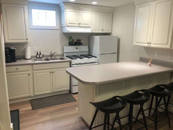 Una cocina moderna con armarios blancos, una isla central con taburetes y electrodomésticos como estufa y refrigerador.