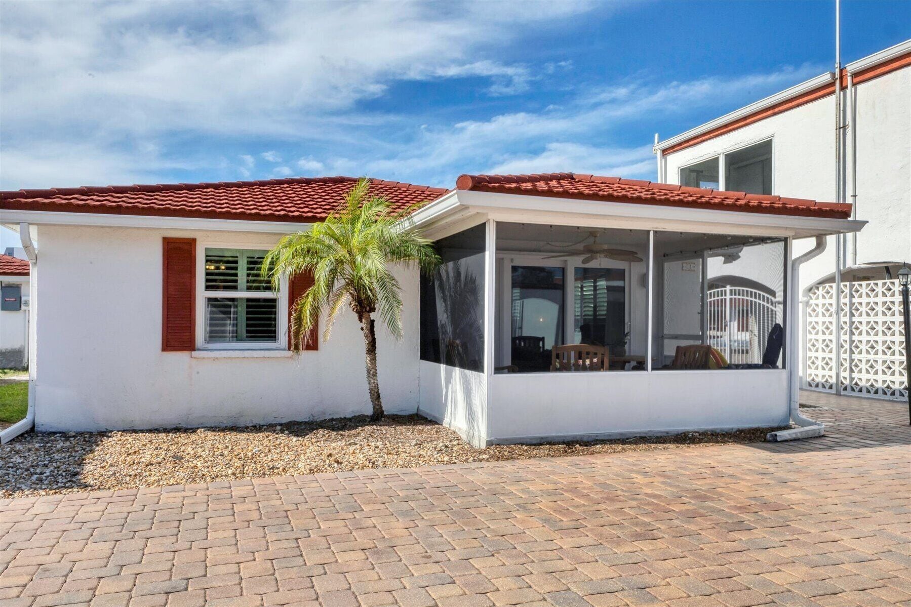 A small, single-story building with a red-tiled roof, a covered patio area, and a palm tree.