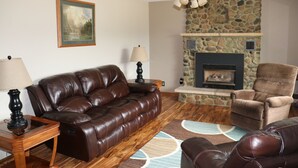 A living room with a brown leather sofa, a brown armchair, a stone fireplace, and a ceiling fan.