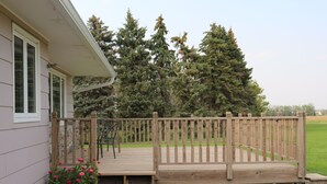 A wooden deck with steps leading to a house, surrounded by a wooden fence and a garden with pink flowers.