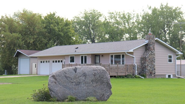 A single-story house with a stone chimney, a garage, and a large rock in the front yard.