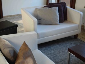 A white sofa with a dark cushion and a light cushion, a small black table, and a grey carpet.