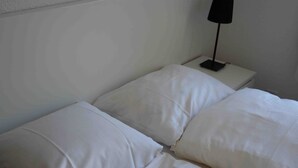 Ein schlichtes Bett mit weißen Laken und einem Nachttisch mit einer Lampe.