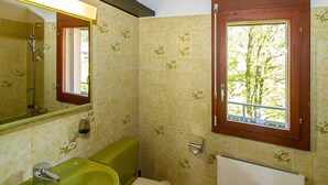 Ein Badezimmer mit einem grünen Waschbecken, einer Toilette, einem Fenster mit Blick auf Bäume und einem Spiegel.