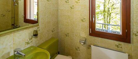 Ein Badezimmer mit einem grünen Waschbecken, einer Toilette, einem Fenster mit Blick auf Bäume und einem Spiegel.