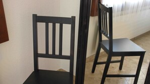Ein schwarzer Sessel mit hoher Rückenlehne und flacher Sitzfläche, platziert in einer Raumecke mit Fliesenboden.