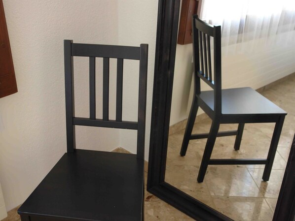A black chair with a high backrest and a flat seat, positioned in a corner of a room with a tiled floor.
