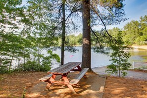 A picnic table by a lake with trees and a white fence in the background. - Couple's Glamping Getaway on Bonny Eagle Pond (Buxton)