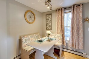 A dining area with a white table, floral-patterned bench, and a window with patterned curtains. - Couple's Glamping Getaway on Bonny Eagle Pond (Buxton)