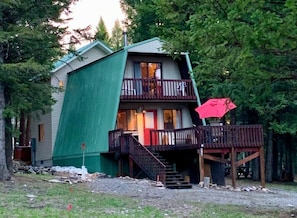 A two-story cabin with a balcony, a staircase, and a red umbrella.