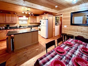 A wooden cabin interior with a kitchen, dining area, and a mirror on the wall.