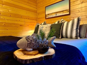 A cozy room with wooden walls, a bed with striped pillows, and a framed picture on the wall.