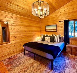 Ein Schlafzimmer in einer Holzhütte mit einem Bett, einer Chandelüster, einem Fenster und einem Gemälde an der Wand.