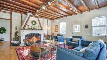 A cozy living room with a fireplace, blue sofas, wooden beams, and a large window.