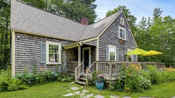 A wooden house with a porch, a small deck, and a garden with stepping stones.