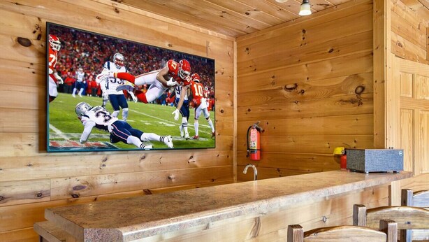 A wooden interior with a bar area, a fire extinguisher, and a television displaying a football game.