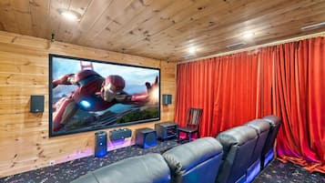 A home theater room with a large flat-screen TV, leather seating, and a red curtain backdrop.