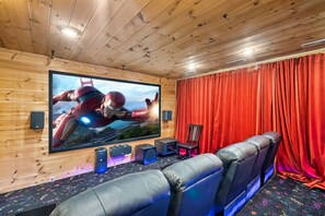 A home theater room with a large flat-screen TV, leather seating, and a red curtain backdrop. - Million $ Views • Theater • Hot Tub • Game Room (Gatlinburg)