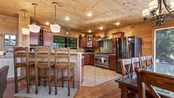 L’intérieur d’un chalet en bois comprend une cuisine, un coin repas et une grande fenêtre donnant sur un paysage verdoyant.