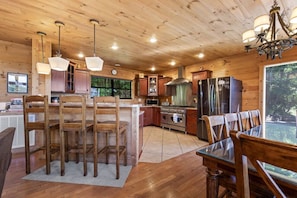 L’intérieur d’un chalet en bois comprend une cuisine, un coin repas et une grande fenêtre donnant sur un paysage verdoyant.