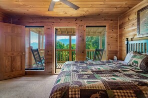 Une chambre avec un grand lit, des murs en bois, un ventilateur de plafond et une vue sur la verdure par les fenêtres.
