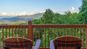 A wooden deck with two Adirondack chairs facing a mountainous landscape.