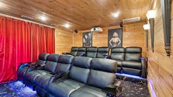 Une salle de cinéma chaleureuse, dotée de fauteuils inclinables en cuir, d’un rideau rouge et de tableaux encadrés aux murs.