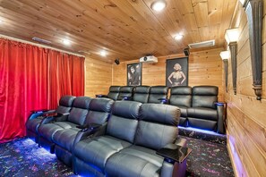A cozy movie theater with leather recliner seating, a red curtain, and framed pictures on the wall. - Million $ Views • Theater • Hot Tub • Game Room (Gatlinburg)