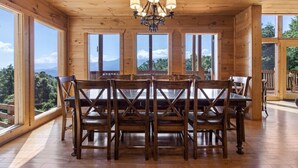A wooden dining room with a chandelier, large windows, and a view of mountains.
