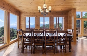 A wooden dining room with a chandelier, large windows, and a view of mountains.