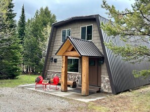 A modern house with a sloped roof, a stone foundation, and a porch with red chairs.