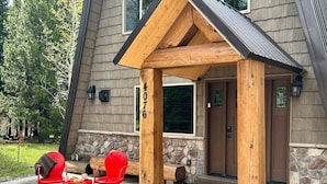 A wooden porch with two red chairs and a small table, a stone fireplace, and a stone wall with a door. - Trailer Parking *Dog Friendly* Fireplace (Island Park)