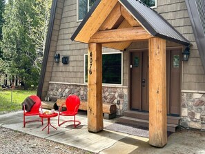 A wooden porch with two red chairs and a table, a stone fireplace, and a house number 4076.