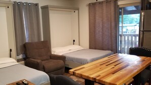 Quarto com duas camas, uma mesa de madeira, uma cadeira e vista para o exterior.