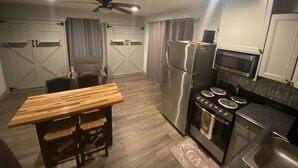 Uma cozinha compacta com geladeira, micro-ondas, fogão e uma mesa de jantar com duas cadeiras.