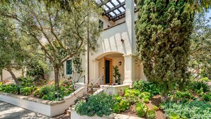 A Mediterranean-style building with a white facade, a covered patio, and a garden with various plants and flowers. - Condo in Trendy Neighborhood Within Walking Distance to Beach! (Santa Barbara)