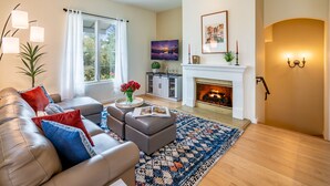 A modern living room with a fireplace, a sofa set, a coffee table with flowers, and a large window with curtains. - Condo in Trendy Neighborhood Within Walking Distance to Beach! (Santa Barbara)