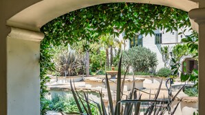 An arched view of a courtyard with a fountain, surrounded by various plants and a building in the background. - Condo in Trendy Neighborhood Within Walking Distance to Beach! (Santa Barbara)