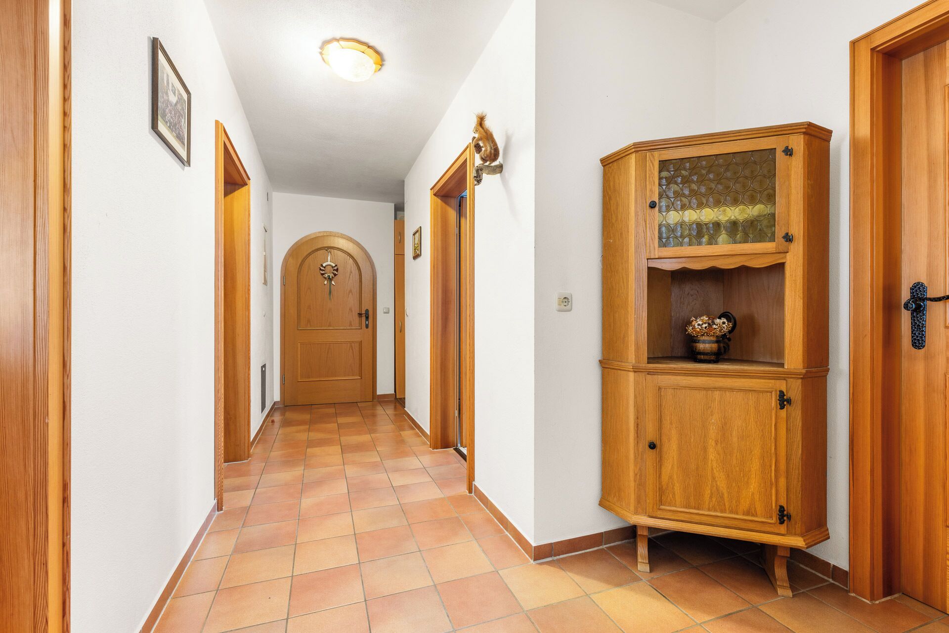 Ein Flur mit Holztüren, Fliesenboden und einem Holzschrank mit Glastüren.